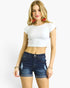 A woman modeling a white short-sleeve crop top and dark blue high-waisted denim shorts with distressed details, set against a plain white background.