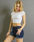 Woman wearing a white crop top and denim shorts against a gray background