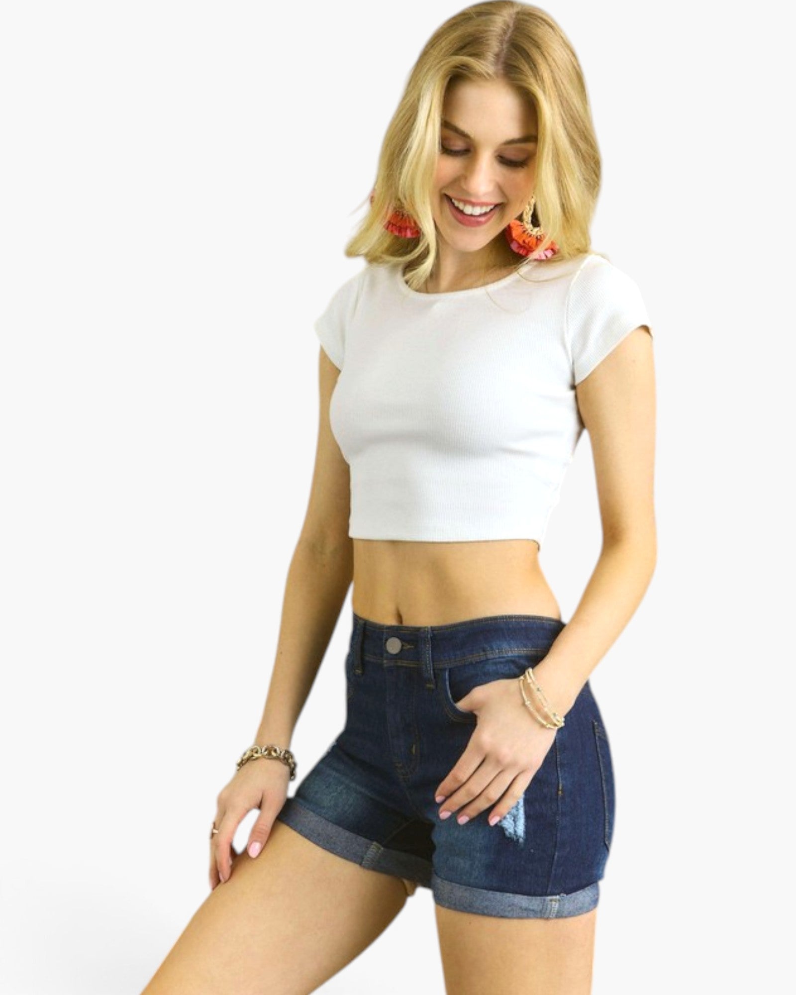A woman modeling a white short-sleeve crop top and dark blue denim shorts against a plain white background.