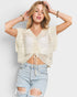 Woman wearing a beige crochet top and ripped jeans against a plain background