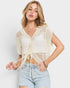 Woman wearing a beige crochet top and light blue jeans on a plain background