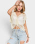 Woman wearing a beige crochet top and ripped jeans on a plain background
