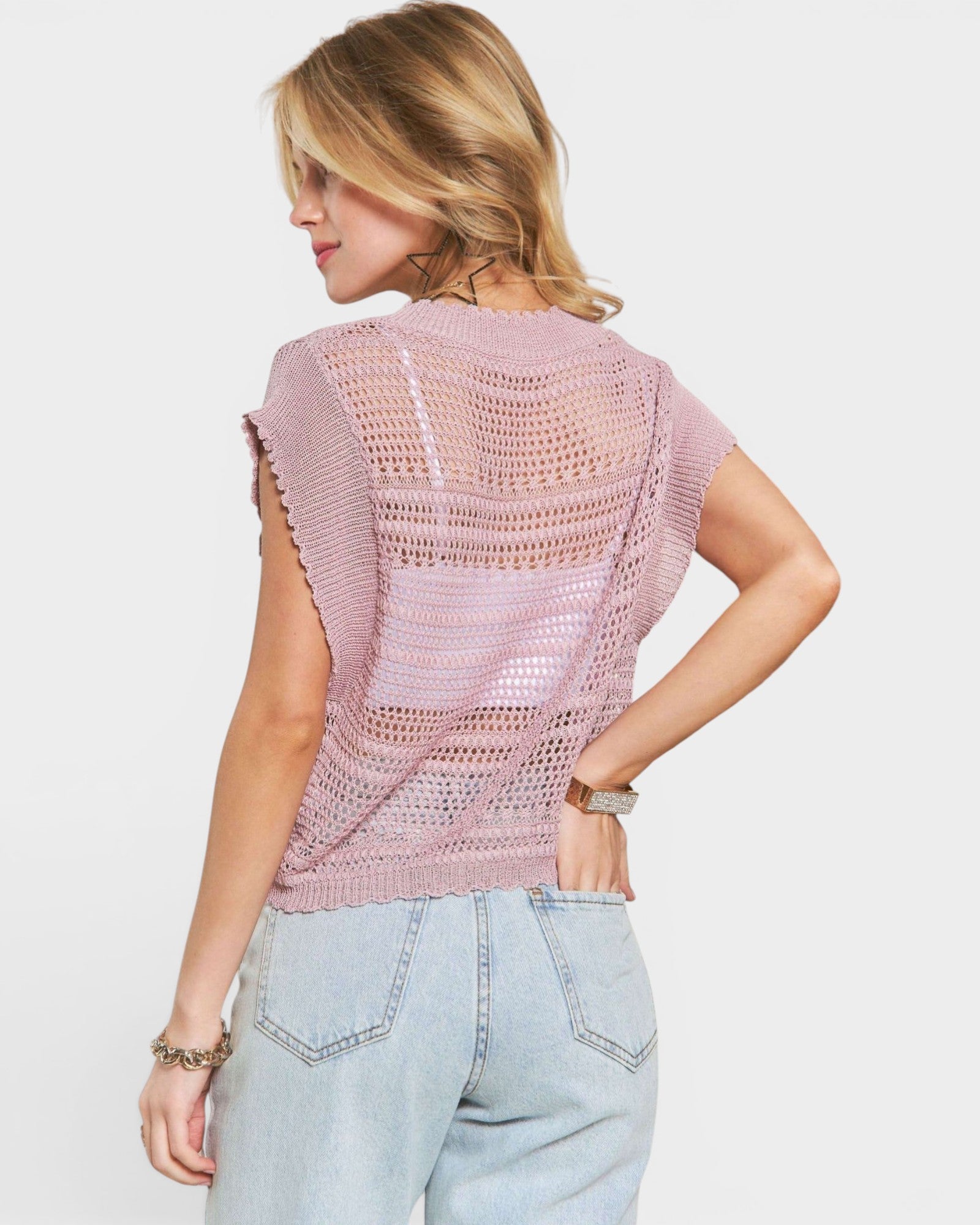 Woman wearing a pink crochet top and light blue jeans on a white background