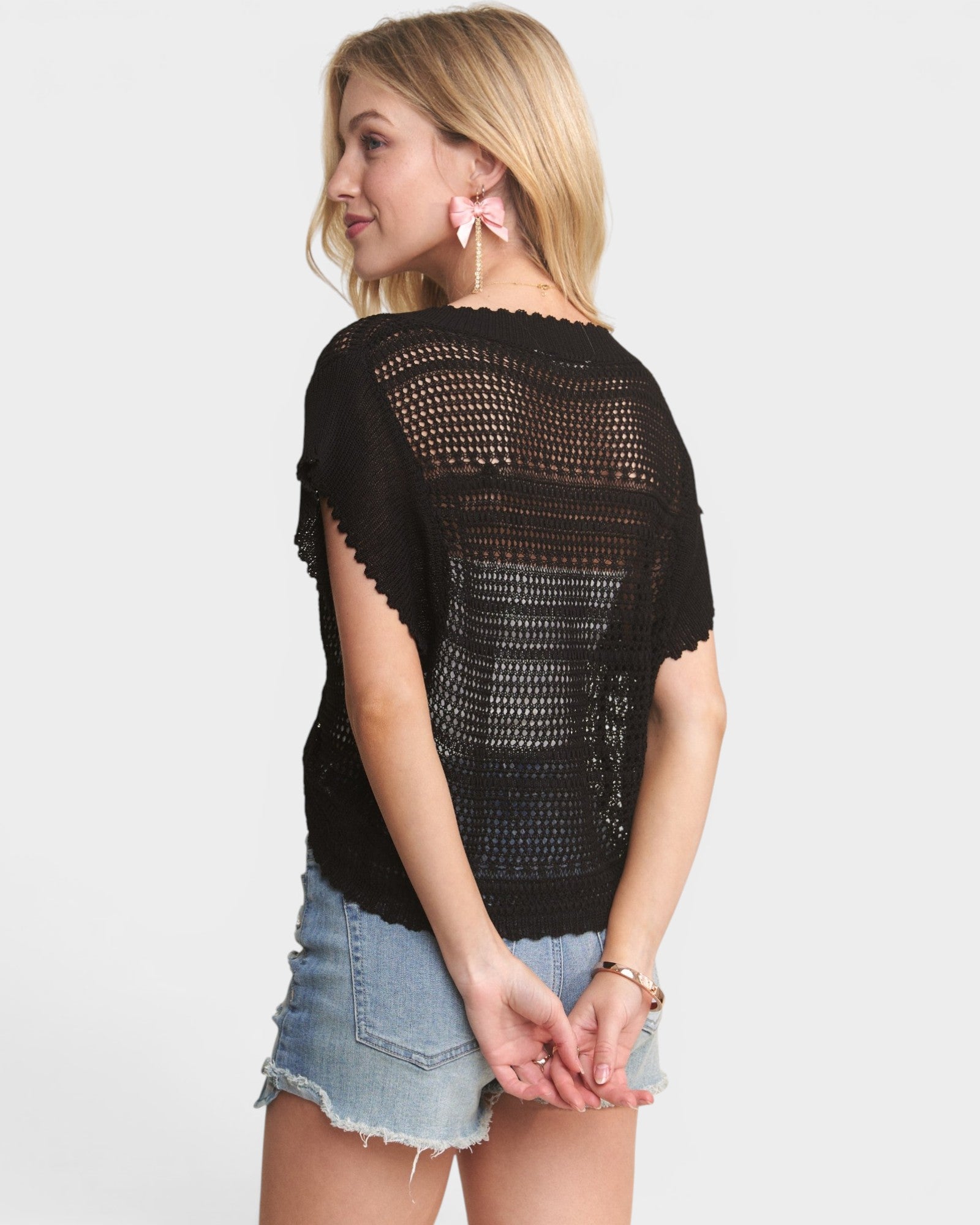 Woman wearing a black crochet top and denim shorts on a white background