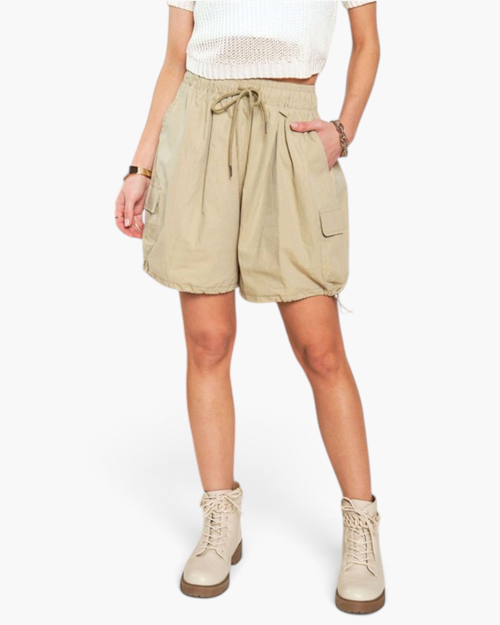 A model wearing beige cargo shorts with a drawstring waist, paired with a white top and beige lace-up boots, shown against a plain white background.