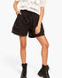 A model wearing black drawstring shorts, a white crochet top, and black lace-up combat boots, shown from the waist down against a light gray studio background.