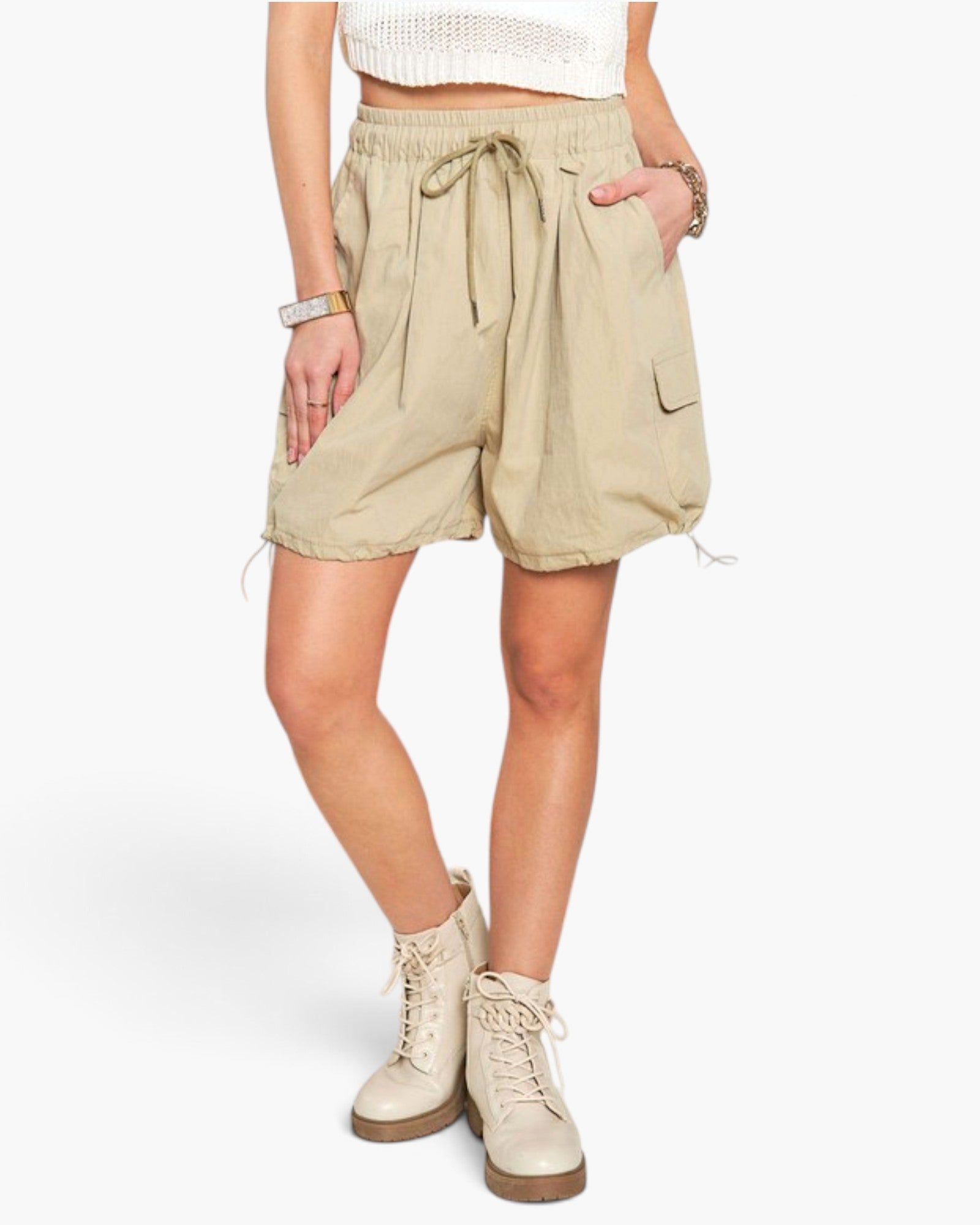 A model wearing beige high-waisted cargo shorts with a drawstring waist, side pockets, and a relaxed fit, paired with beige lace-up boots against a plain white background.