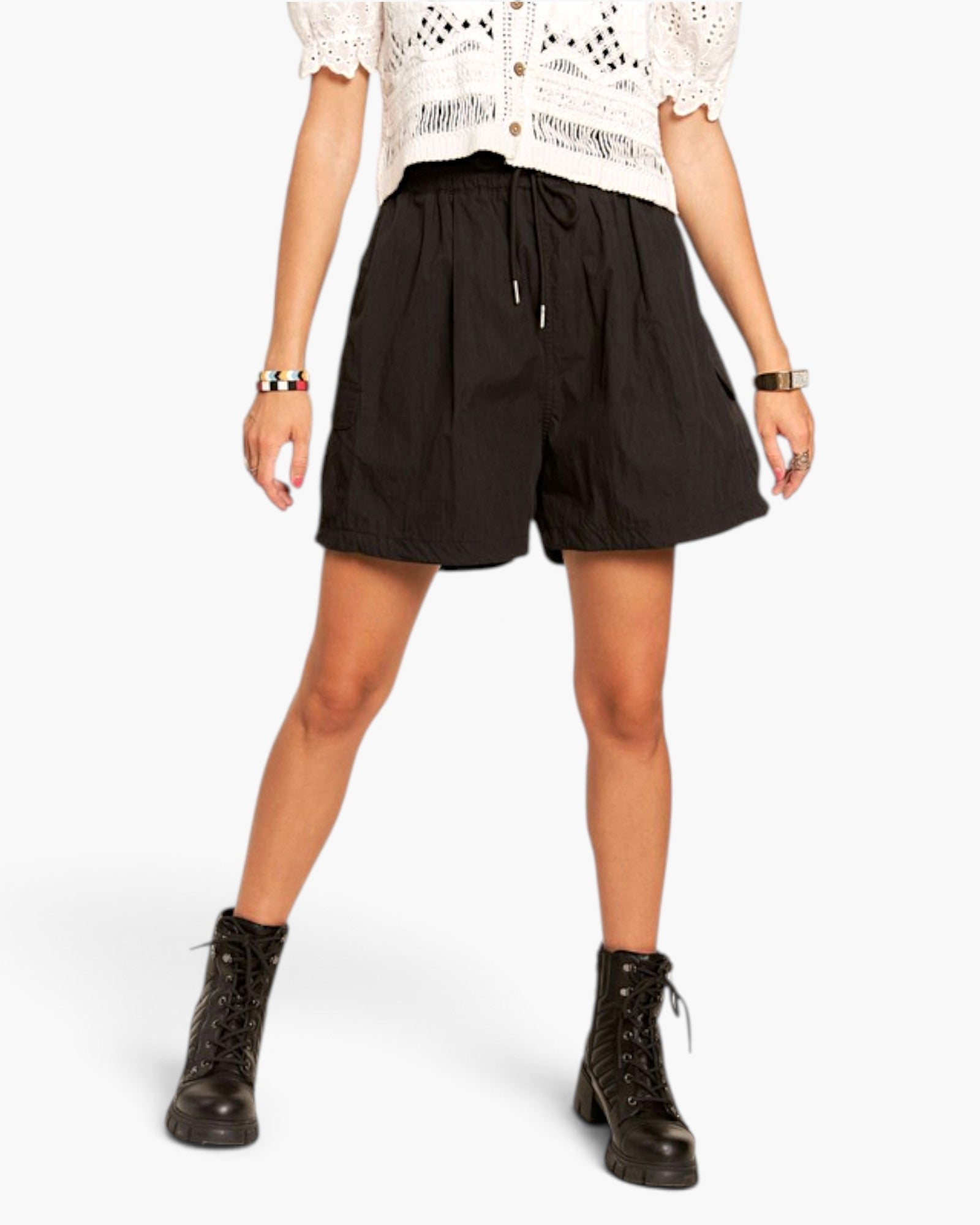 A model wearing black drawstring shorts, a white crochet top, and black lace-up combat boots, photographed against a clean white studio background.