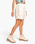 A model wearing off-white cargo shorts with side pockets and drawstrings, paired with matching off-white lace-up boots and a colorful patterned crop top, shown against a plain light gray background.