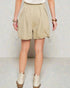 Person wearing beige shorts and white shoes on a plain background