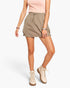 A model wearing a light brown utility mini skirt with a drawstring waist, paired with a pink ribbed top and beige lace-up boots, set against a plain white studio background.
