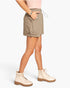 A model wearing a light brown utility mini skirt with a drawstring waist and side pockets, paired with cream combat boots and a light pink top, shown from the waist down on a white studio background.