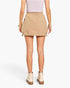 A model from the back wearing a beige cargo mini skirt, a light pink ribbed top, and beige ankle boots, set against a plain white studio background.