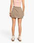 A model from the back wearing a light brown mini skirt with cargo pockets, paired with a light pink top and beige ankle boots, against a plain white background.