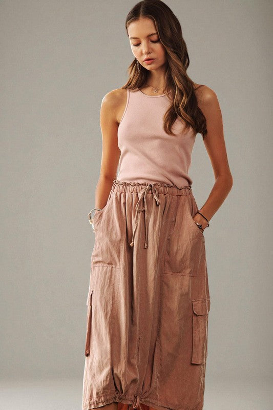 Woman wearing a pink sleeveless top and brown wide-leg pants against a plain background
