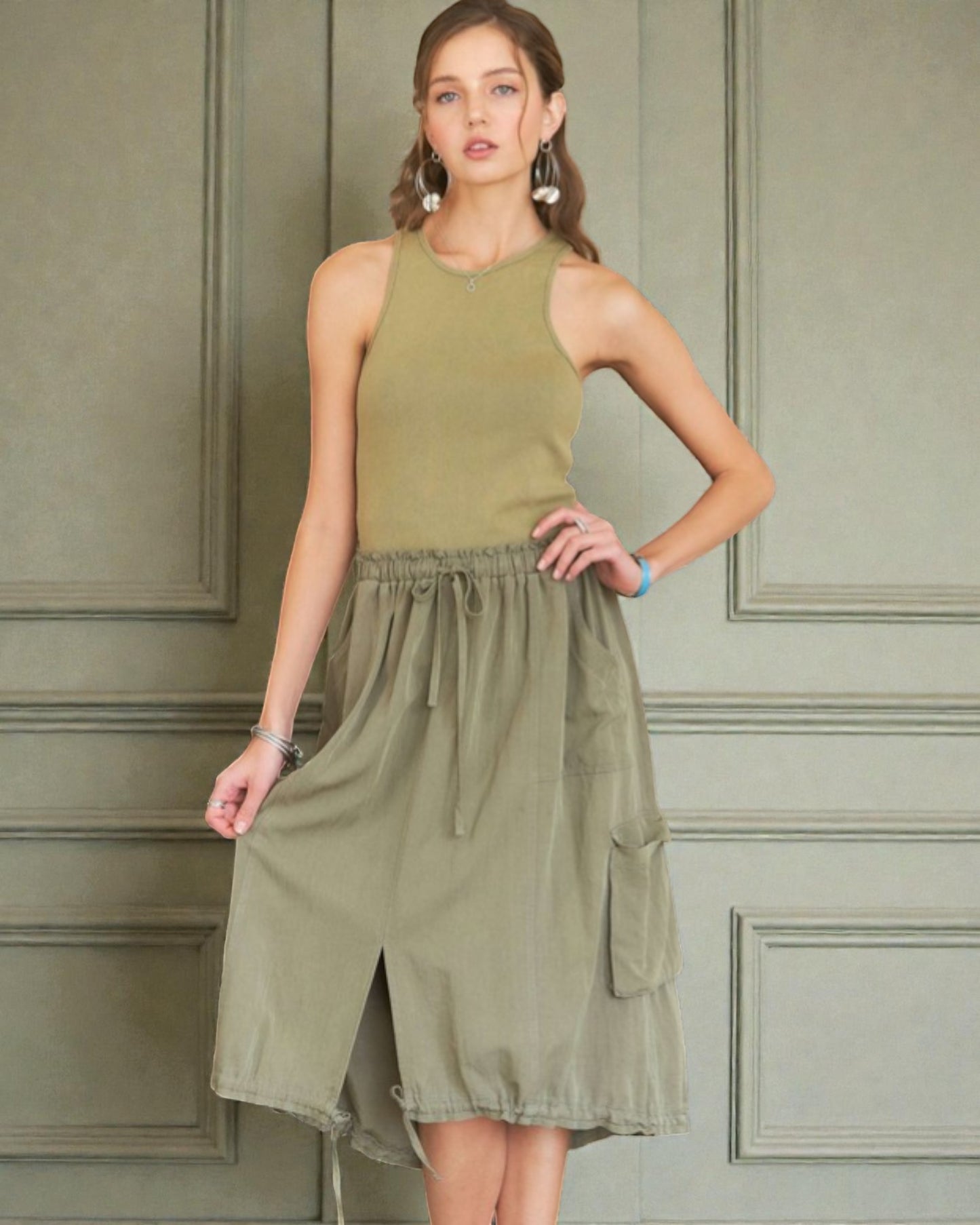 Woman wearing an olive green dress against a paneled wall.