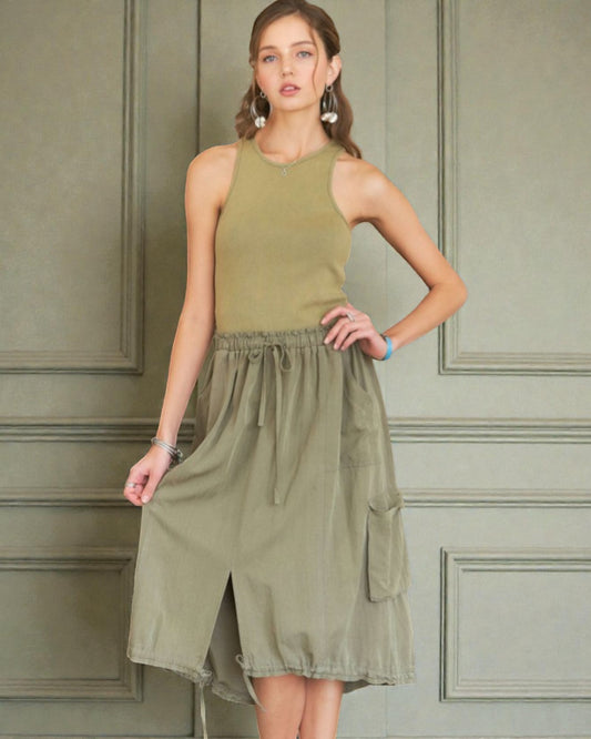 Woman wearing an olive green dress against a paneled wall.