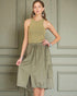 Woman wearing an olive green dress against a paneled wall.