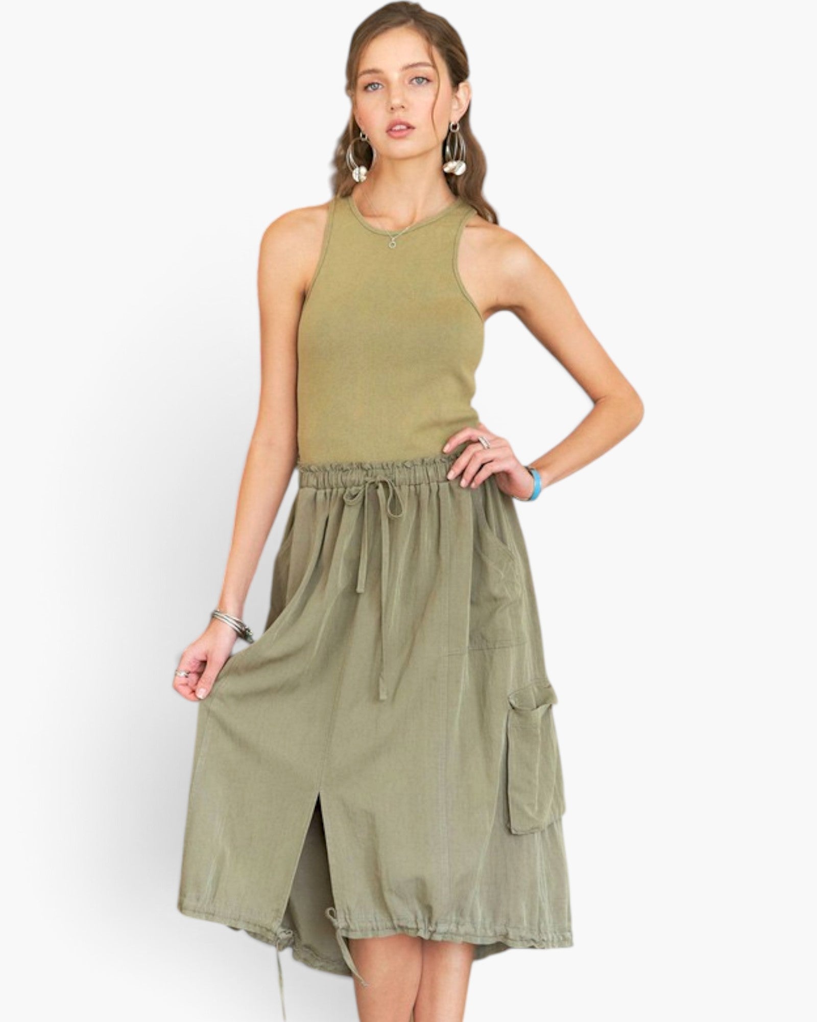 A woman modeling a sleeveless olive green dress with a ribbed knit top section, elastic drawstring waist, and side cargo pockets, set against a plain light gray background.
