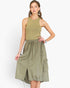 A woman modeling a sleeveless olive green dress with a ribbed knit top section, elastic drawstring waist, and side cargo pockets, set against a plain light gray background.