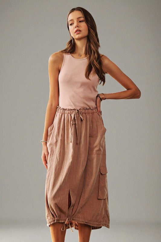 Woman wearing a pink sleeveless dress with a drawstring waist on a gray background