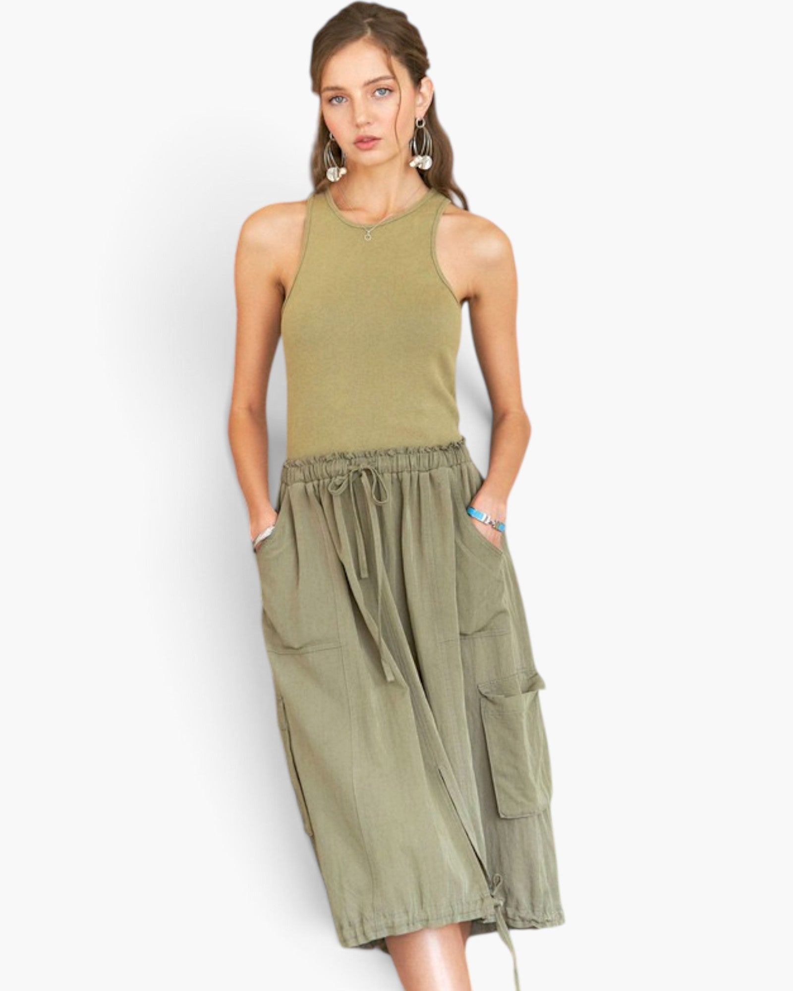 A woman modeling a sleeveless olive green knit top paired with an olive green high-waisted midi skirt featuring cargo pockets and a drawstring waist, set against a plain light gray background.