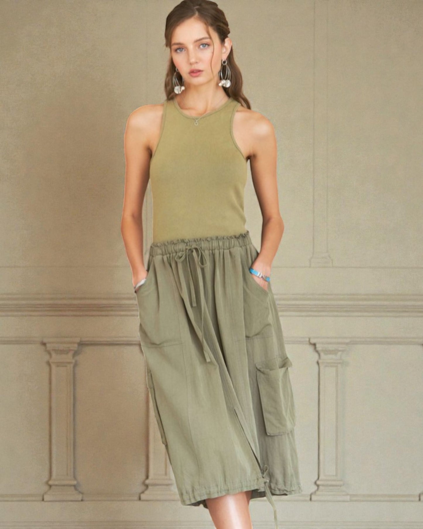 Woman wearing a green sleeveless dress against a beige wall.