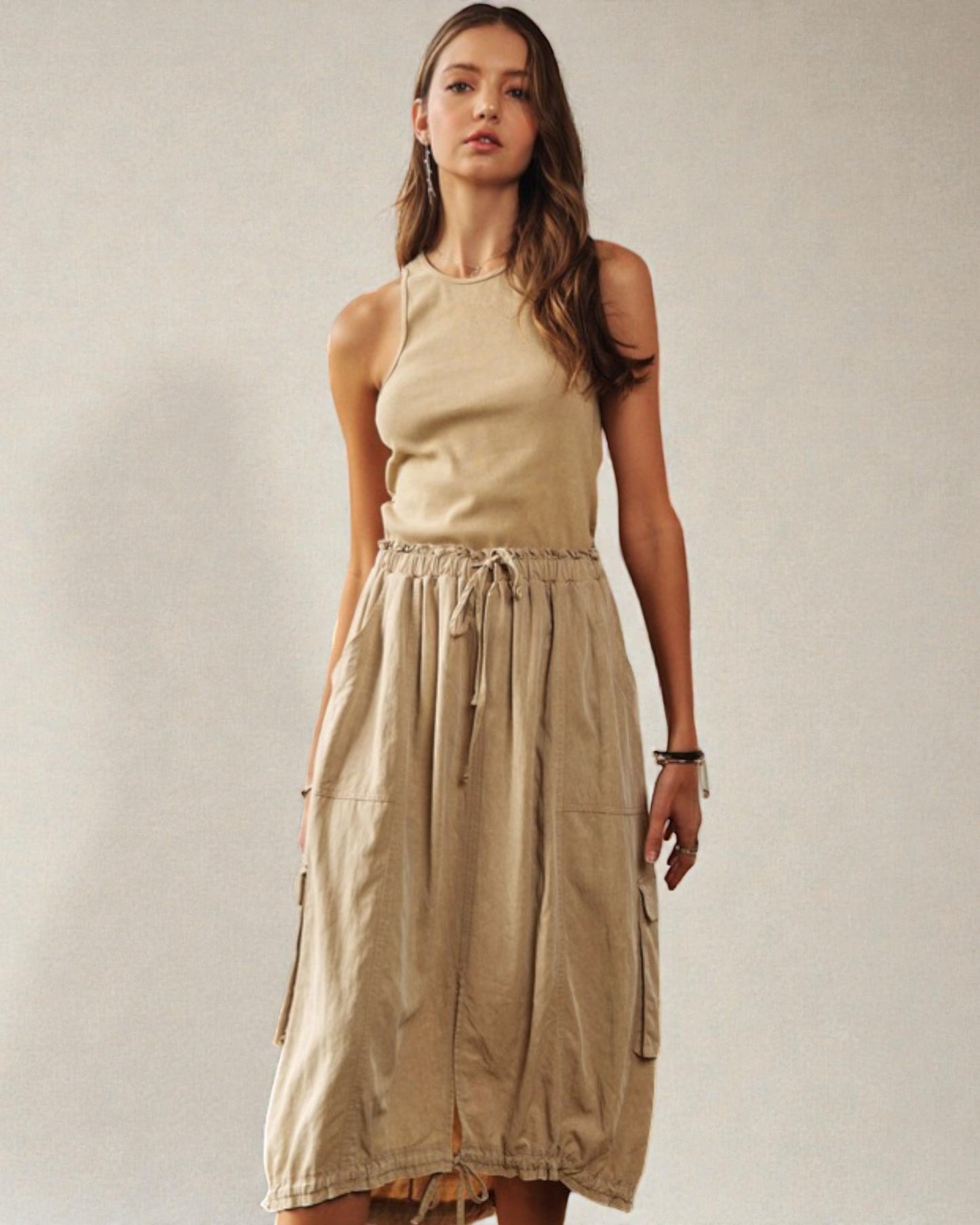 Woman wearing a beige sleeveless top and skirt against a plain background