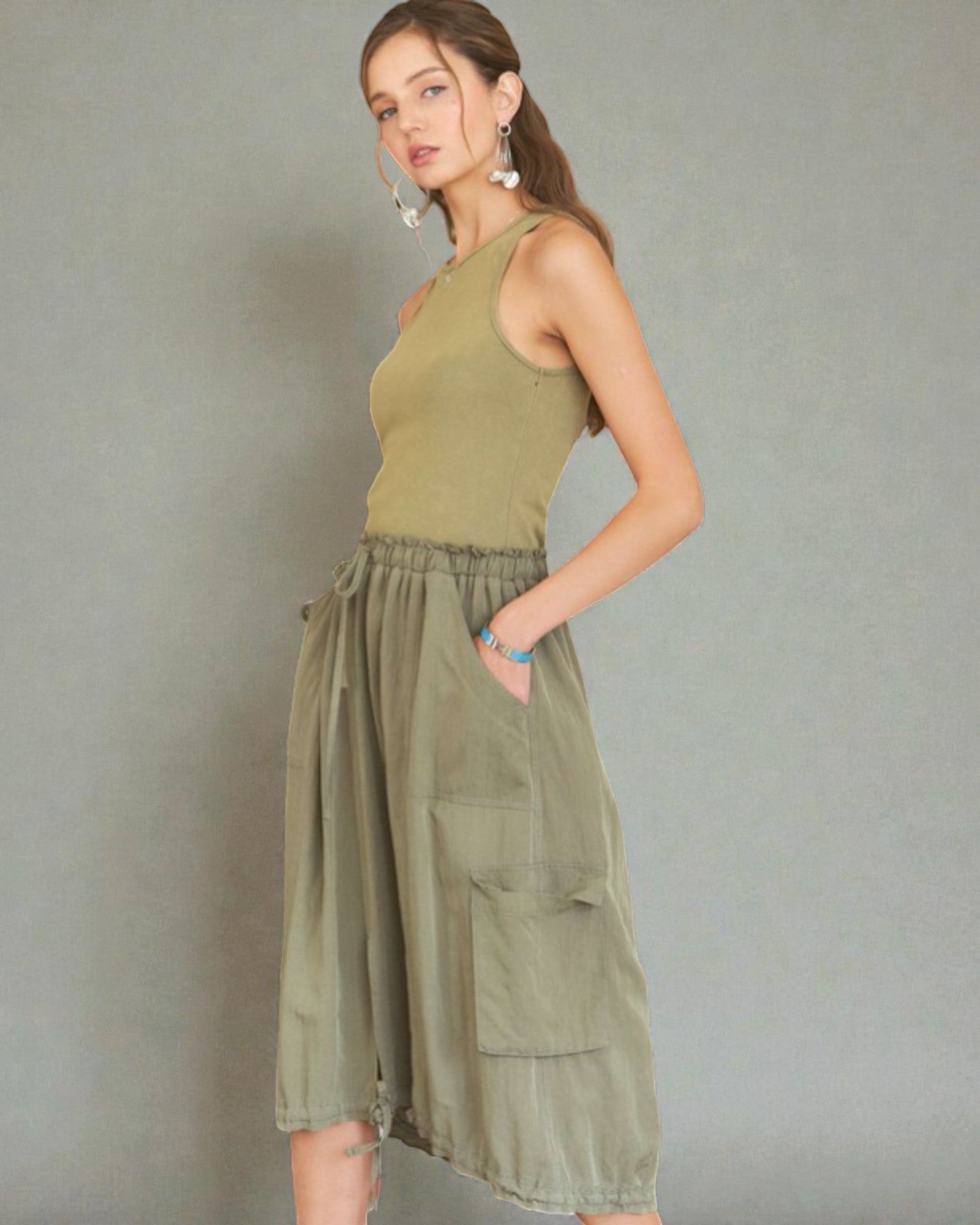 Woman wearing a green sleeveless dress with cargo pockets against a gray background