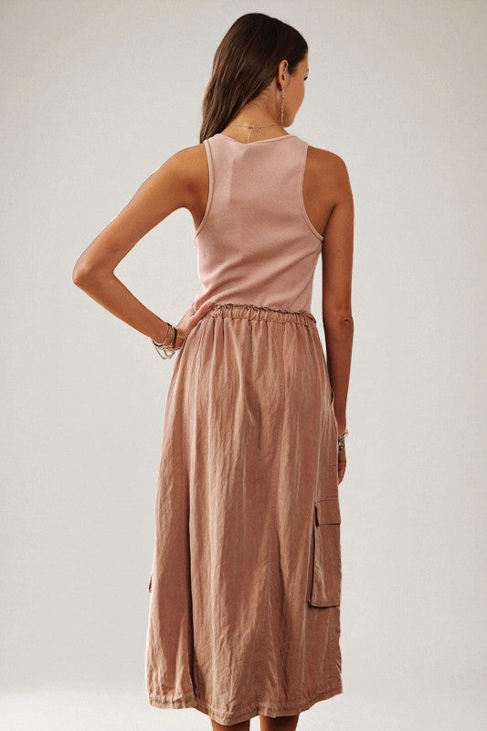 Woman wearing a pink sleeveless top and brown skirt against a plain background