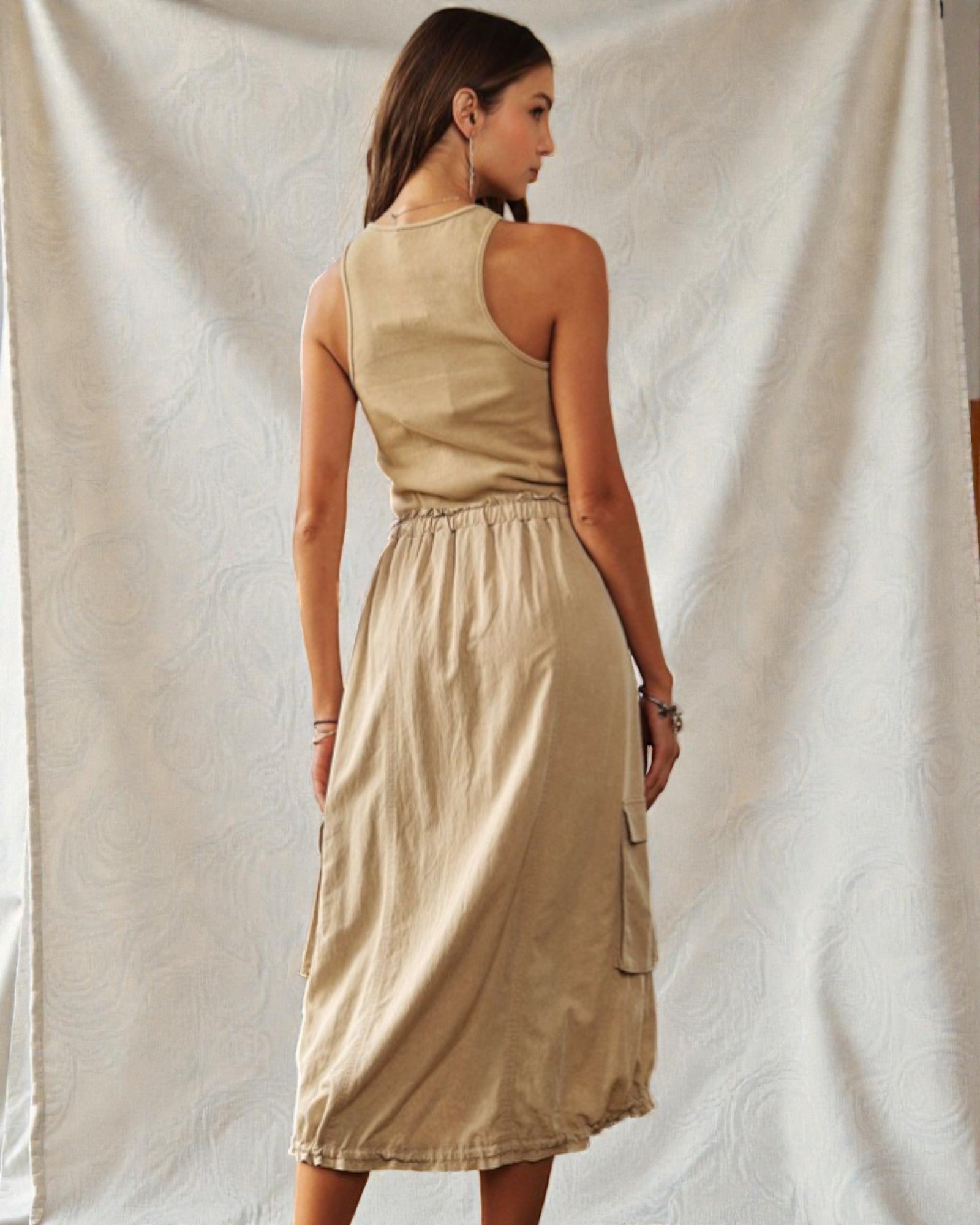 Woman wearing a beige sleeveless dress against a white curtain background