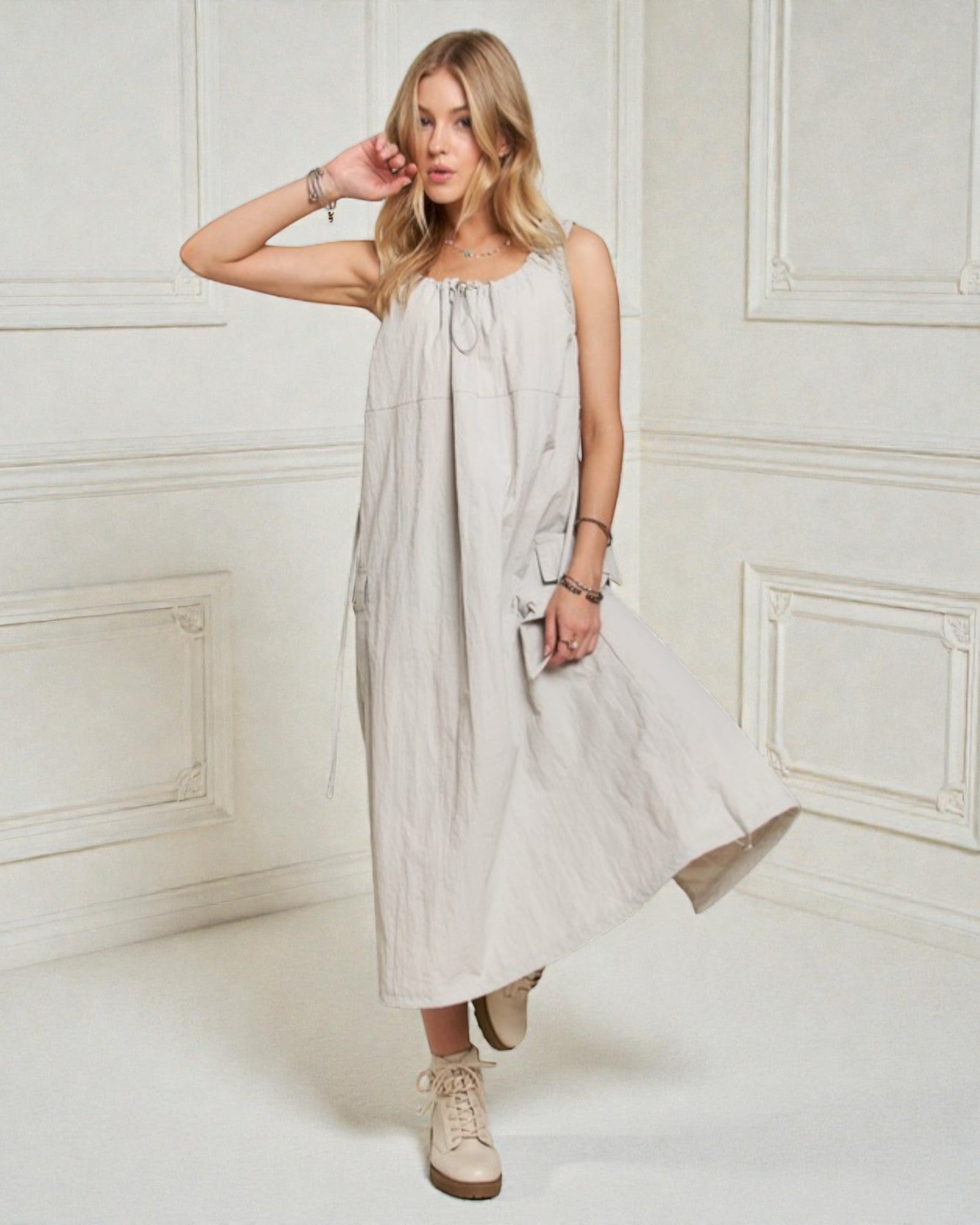 Woman wearing a light gray sleeveless dress in a white room.