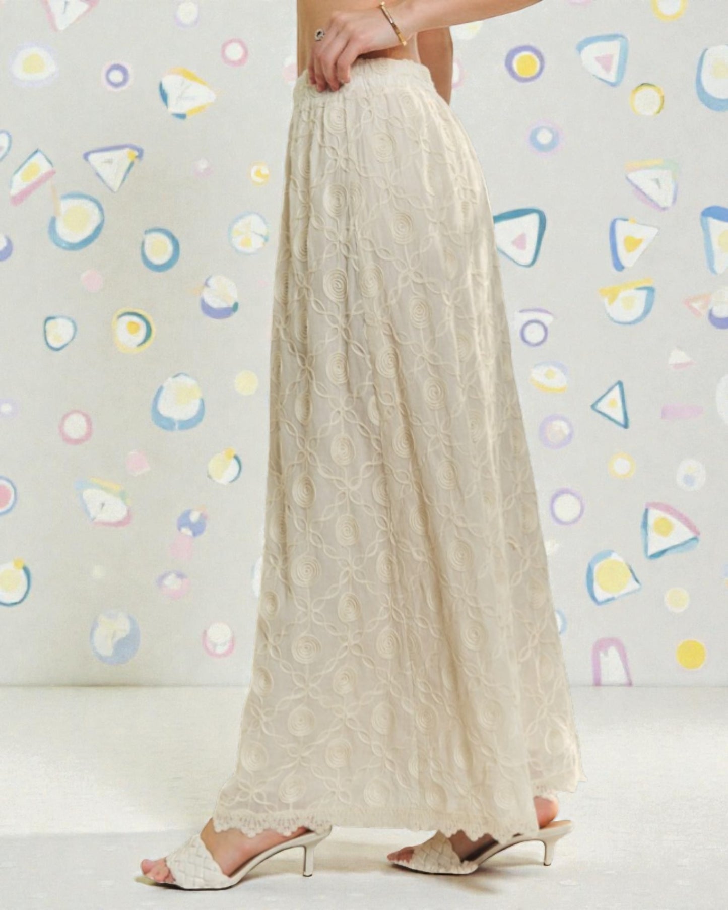 Beige wide-leg pants worn by a person against a colorful abstract wall.