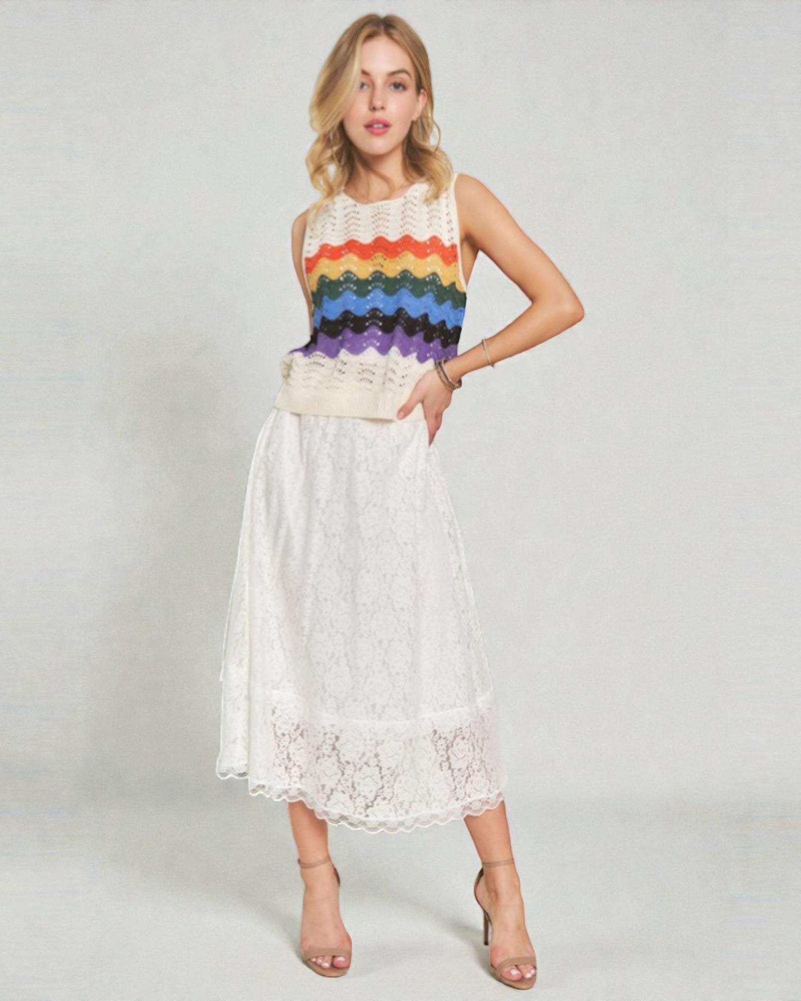 Woman wearing a sleeveless rainbow-patterned top and white lace skirt on a plain background