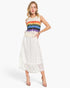 A woman modeling a sleeveless knit top with a rainbow stripe pattern and a white lace midi skirt, paired with nude high-heeled sandals against a light gray studio background.