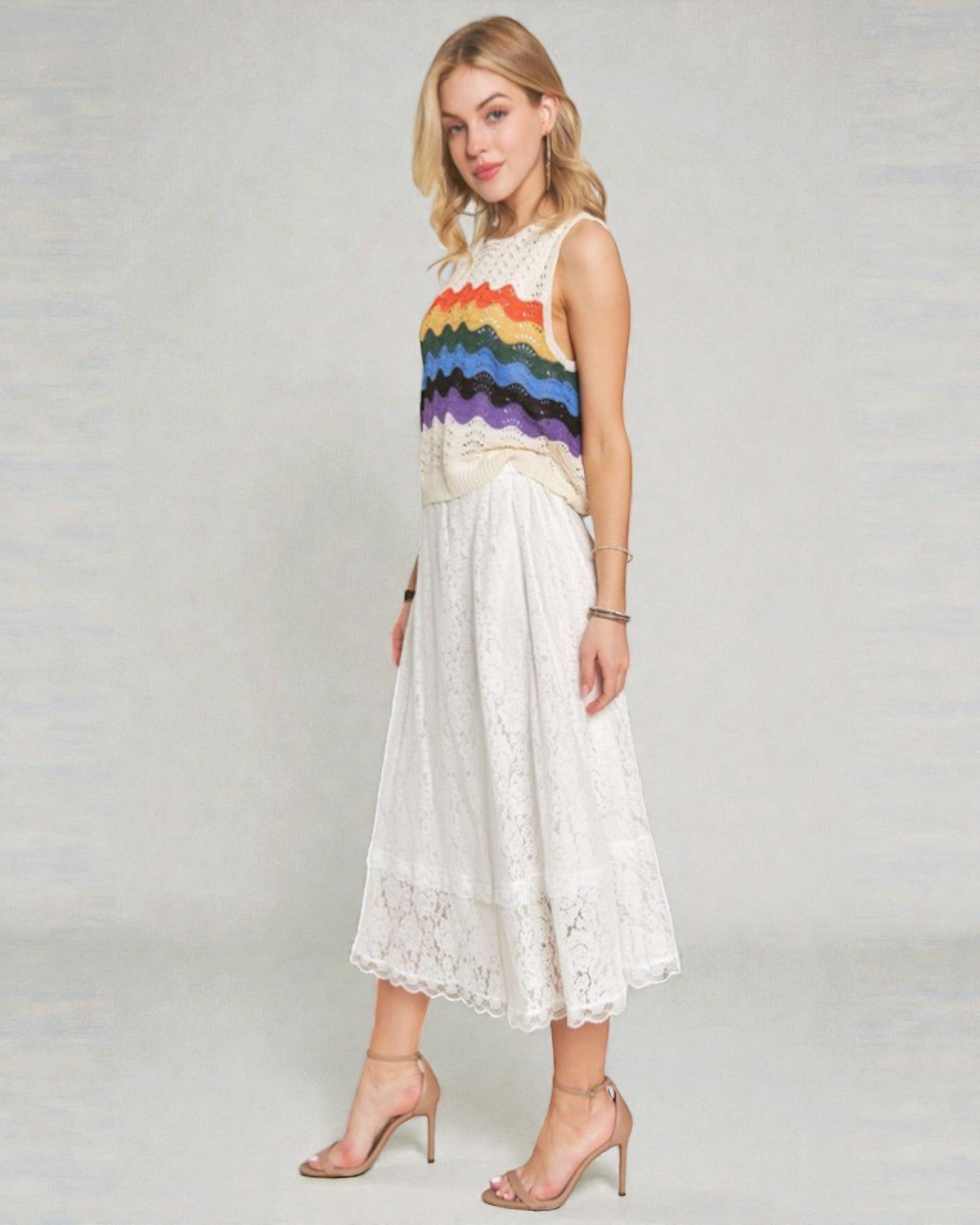 Woman wearing a sleeveless rainbow striped top and white skirt on a plain background