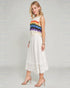 Woman wearing a sleeveless rainbow striped top and white skirt on a plain background