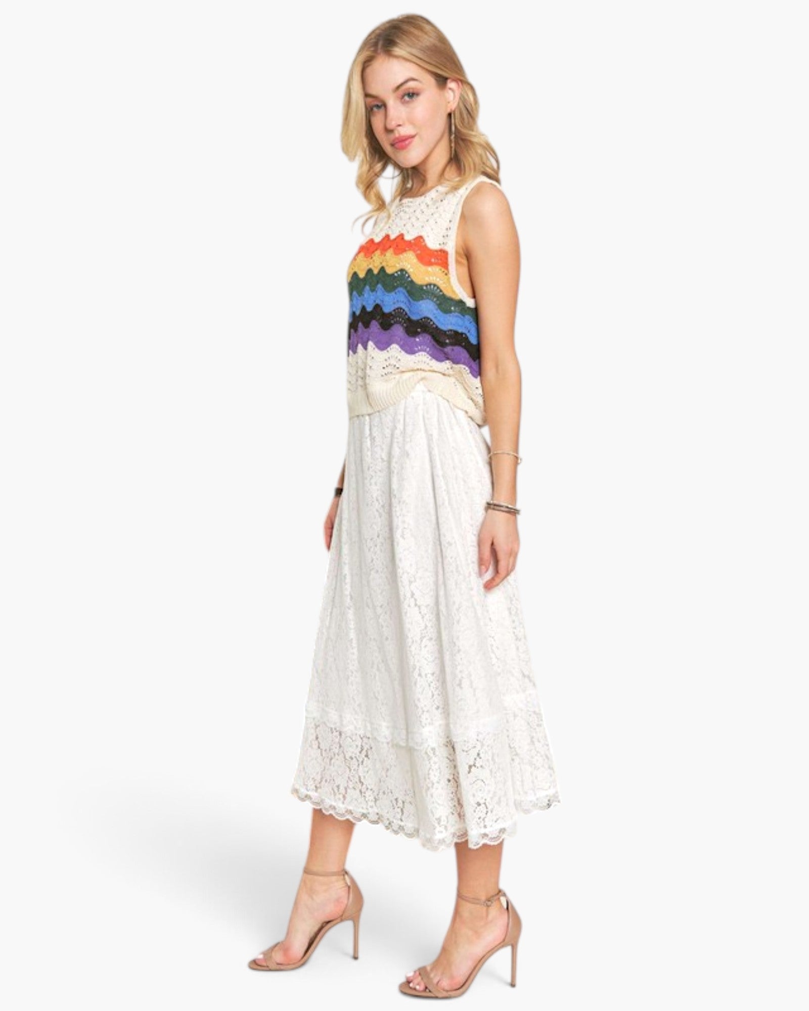 A woman modeling a sleeveless midi dress with a cream lace skirt and a colorful rainbow-striped bodice, paired with nude high-heeled sandals against a light gray studio background.