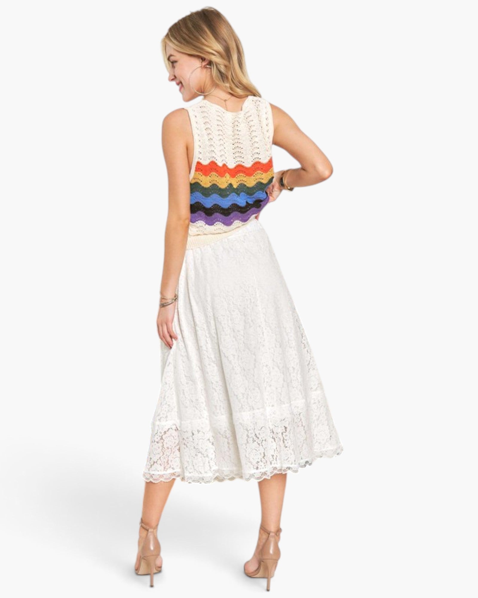 A woman modeling a sleeveless white crochet midi dress from the back, featuring a colorful rainbow-striped knit band across the upper back and white lace skirt, against a light gray studio background.