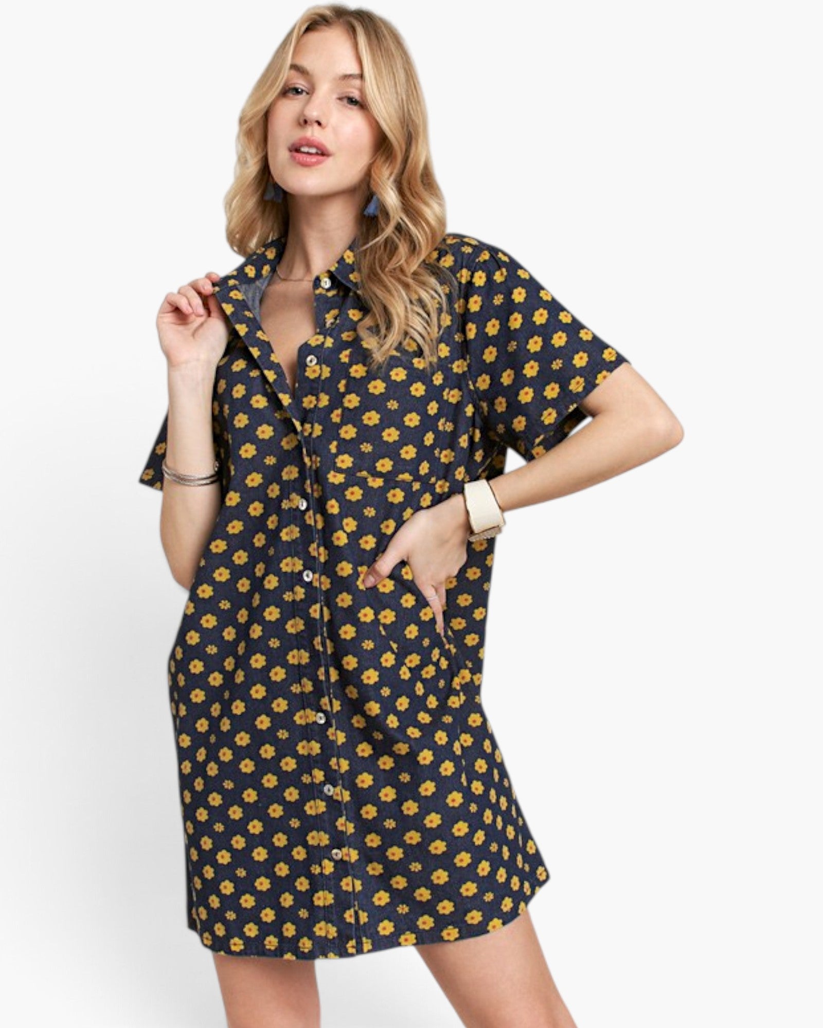 A woman modeling a short-sleeve button-front shirt dress with a navy base and yellow floral print, photographed against a clean light gray studio background.