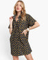 A woman modeling a short-sleeve button-front shirt dress with a navy base and yellow floral print, photographed against a clean light gray studio background.