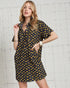 Woman wearing a navy dress with yellow floral pattern against a white brick wall.