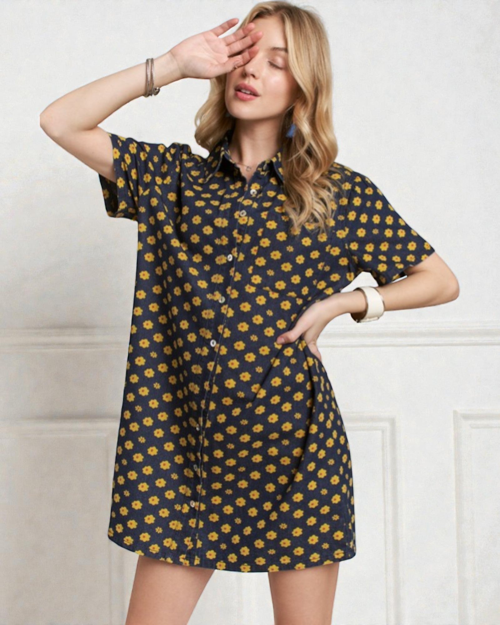 Woman wearing a navy dress with yellow floral pattern against a white wall.