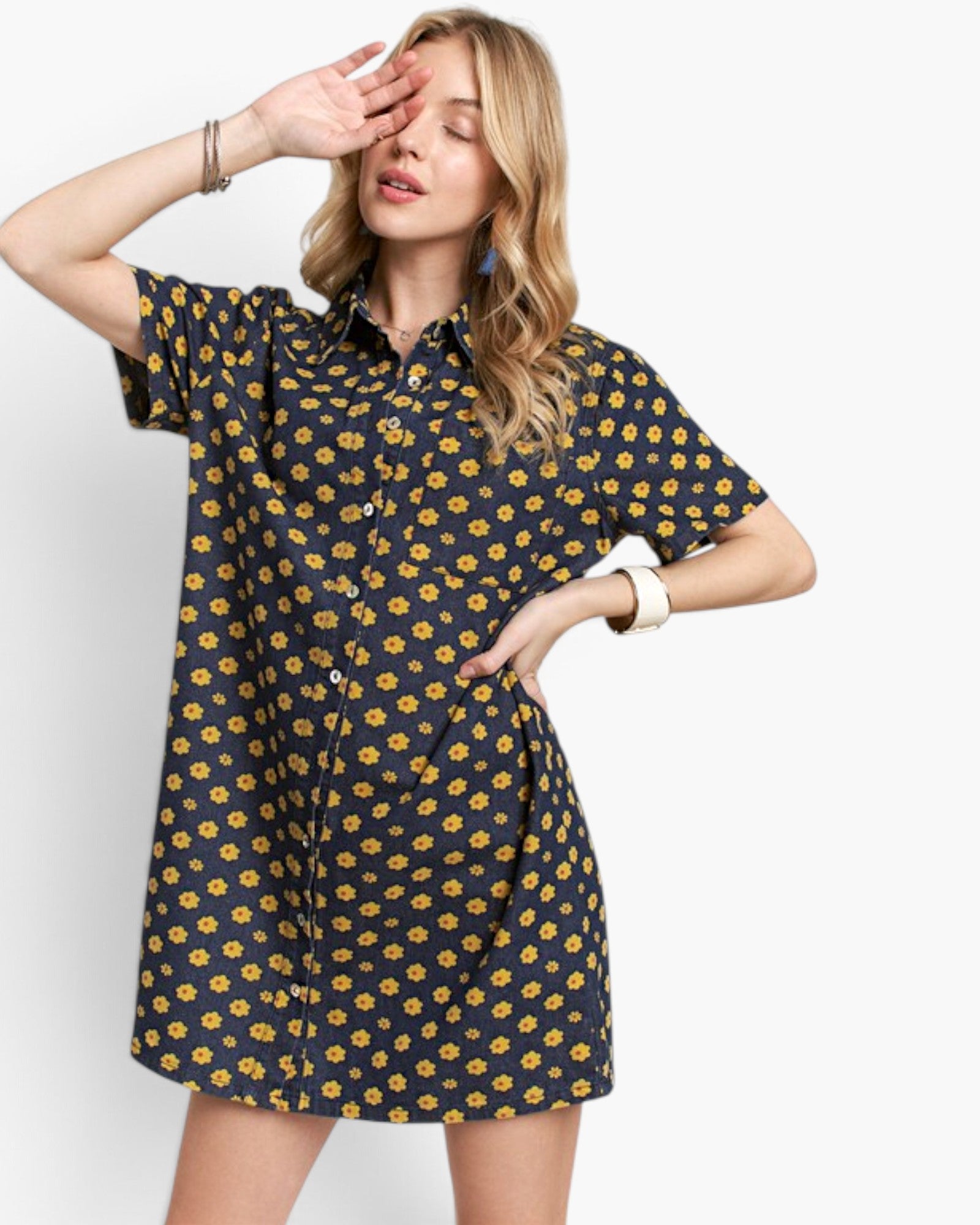 A woman modeling a short-sleeve button-up shirt dress with a dark navy blue base and a yellow floral pattern, set against a plain white studio background.