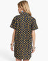 A woman shown from the back wearing a short-sleeve collared shirt dress with a repeating yellow flower print on a dark navy background, against a light gray studio background.