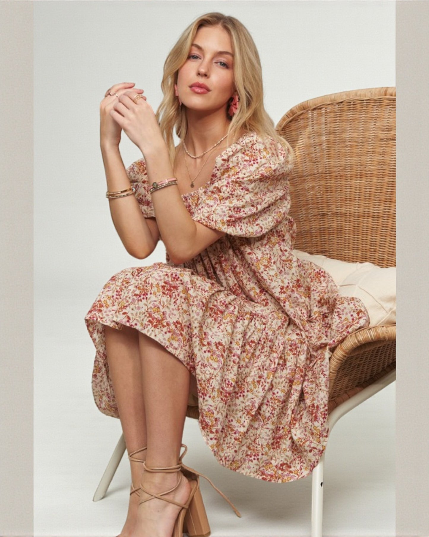 Woman in a floral dress sitting on a wicker chair against a plain background