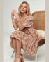 Woman in a floral dress sitting on a wicker chair against a plain background