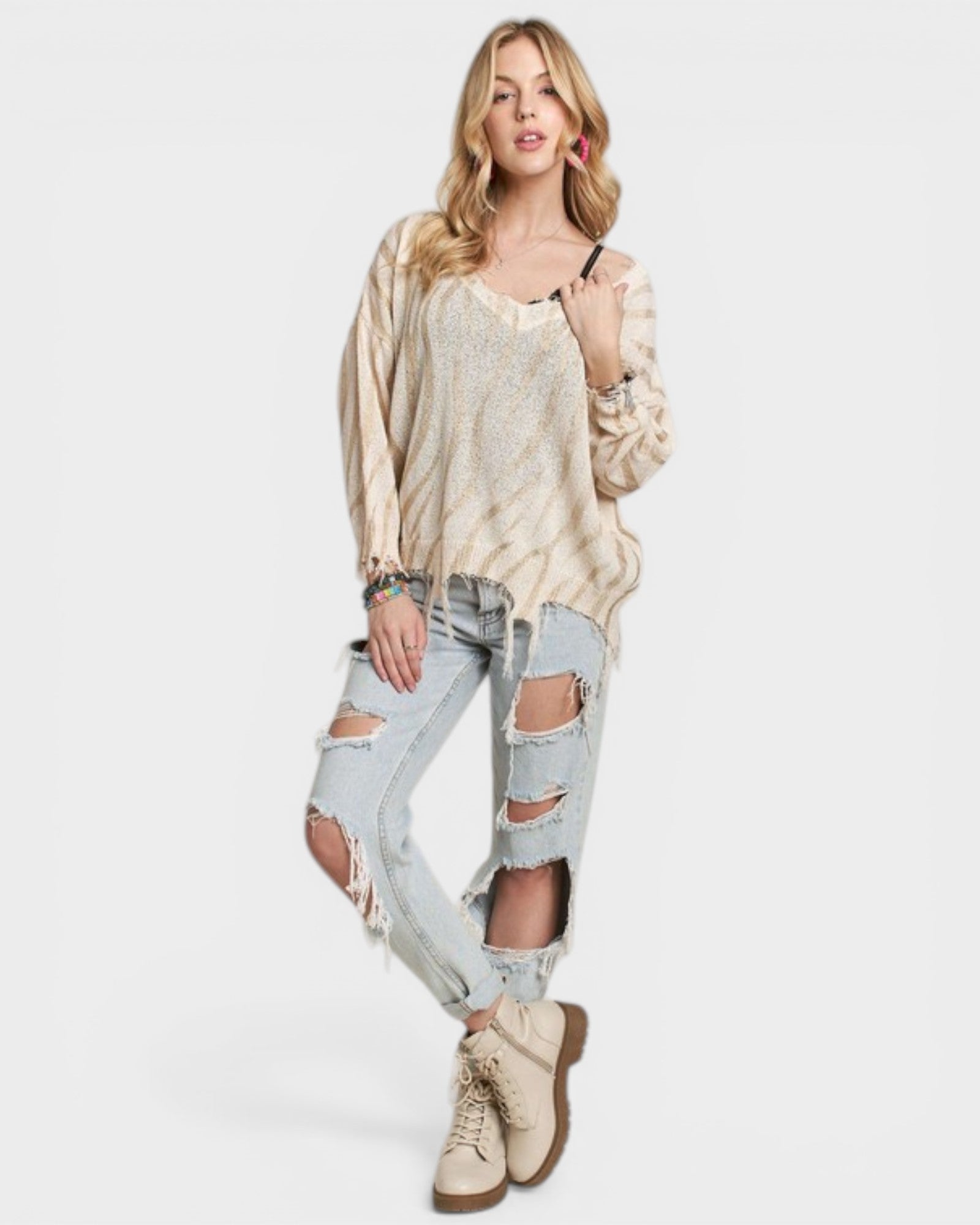 Woman wearing a beige sweater and ripped jeans on a white background