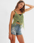 Woman wearing a green crochet top and denim shorts on a white background