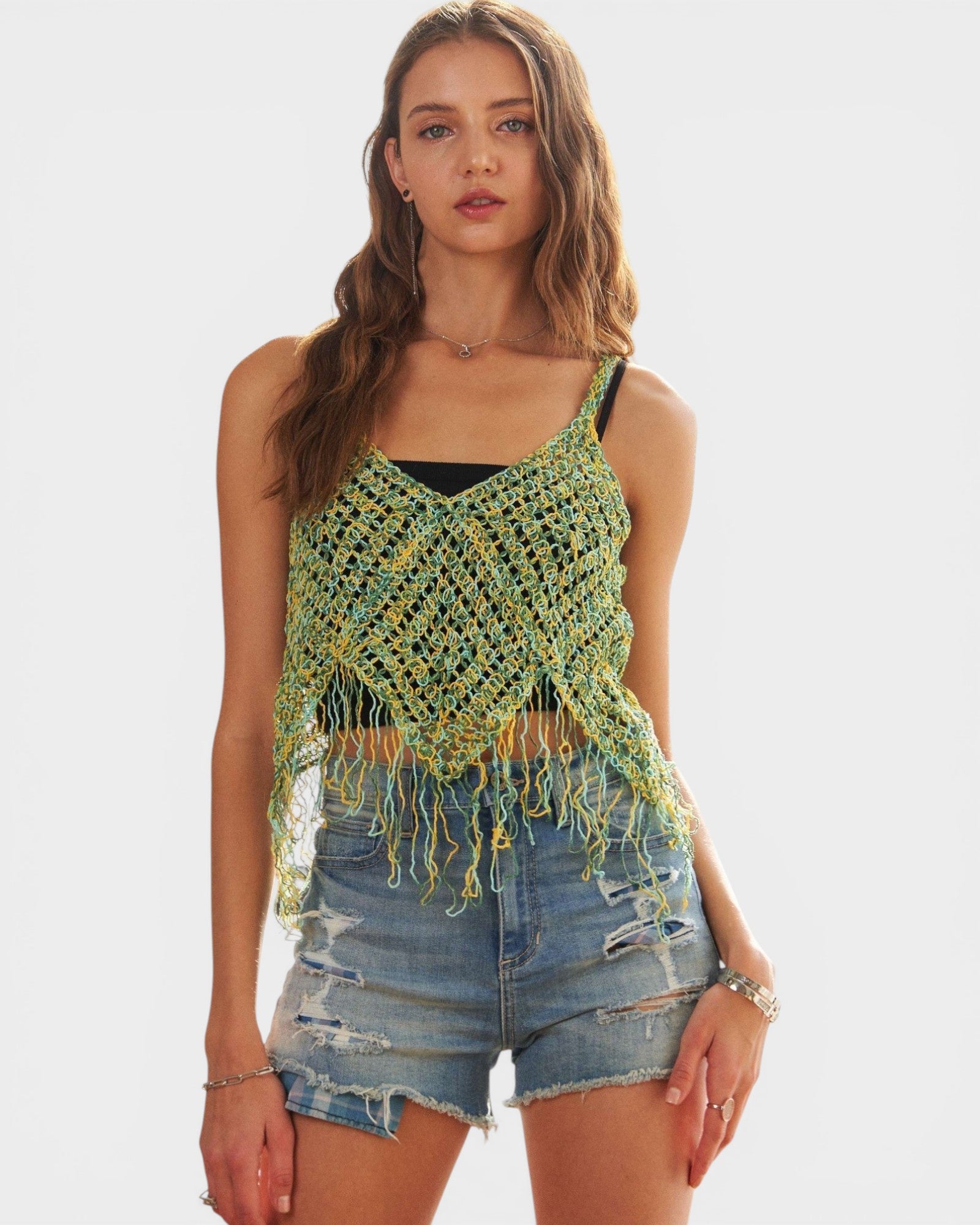 Woman wearing a green crochet top with fringes and denim shorts on a white background